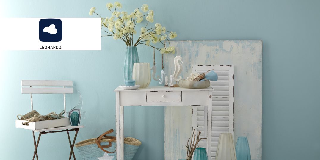 Een mediterraan interieur met een witte tafel met vazen en decoraties van het merk Leonardo tegen een zachtblauwe muur.