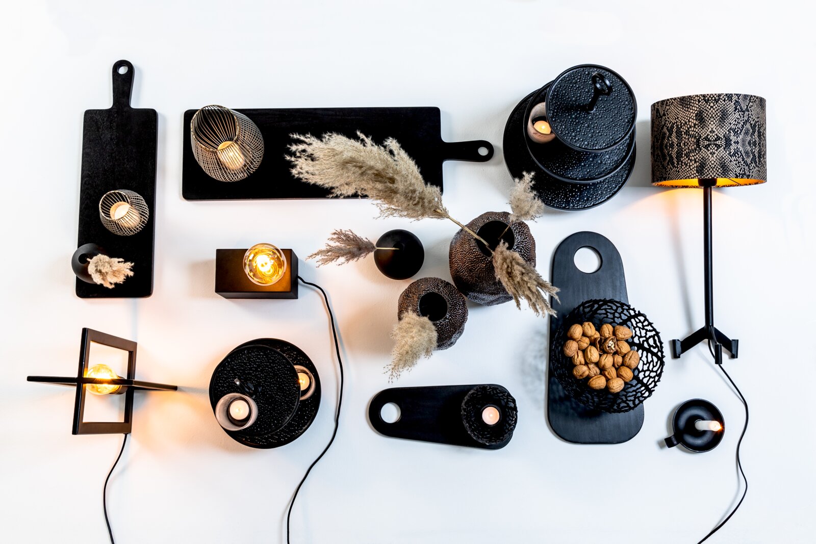 Stilvolles Wohnaccessoire-Arrangement in Schwarz mit Lampen, Kerzenhaltern, Dekotabletts, Vasen, Pampasgras und Nussschale aus der Vogelperspektive
