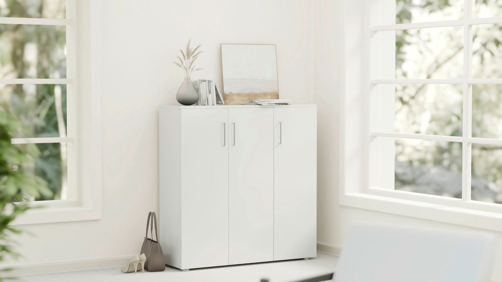 Weißer Schuhschrank mit drei Türen in einer Ecke eines hellen Raumes, dekoriert mit einer Vase, Büchern und einem Bild auf der Oberseite, seitliche Perspektive