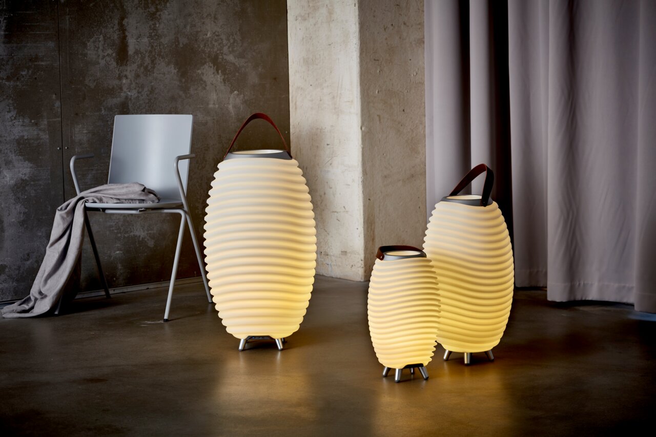 Drei Akku-Leuchten in verschiedenen Größen mit wellenförmigem Design und Tragegriff, auf einem Boden stehend, seitliche Perspektive.