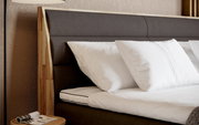 Nahaufnahme eines Boxspringbetts mit dunklem Kopfteil und weißen Kissen, seitliche Perspektive.