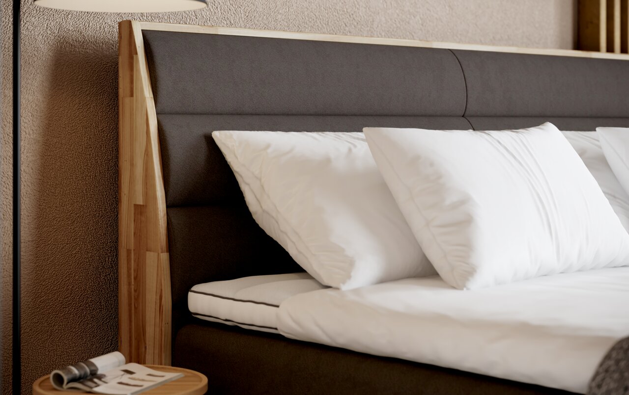 Nahaufnahme eines Boxspringbetts mit dunklem Kopfteil und weißen Kissen, seitliche Perspektive.