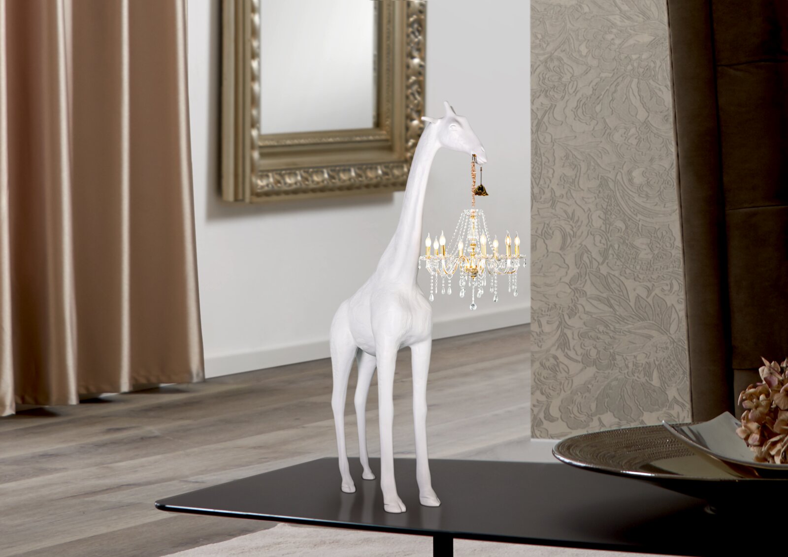 Weiße Giraffen-Dekofigur auf schwarzem Couchtisch, seitliche Ansicht, hält einen kleinen Kristall-Kronleuchter im Maul in modernem Wohnraum