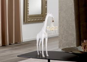 Weiße Giraffen-Dekofigur auf schwarzem Couchtisch, seitliche Ansicht, hält einen kleinen Kristall-Kronleuchter im Maul in modernem Wohnraum