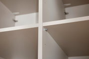 Nahaufnahme eines weißen, vierteiligen Kleiderschranks mit Regalböden, aus der Innenperspektive fotografiert.