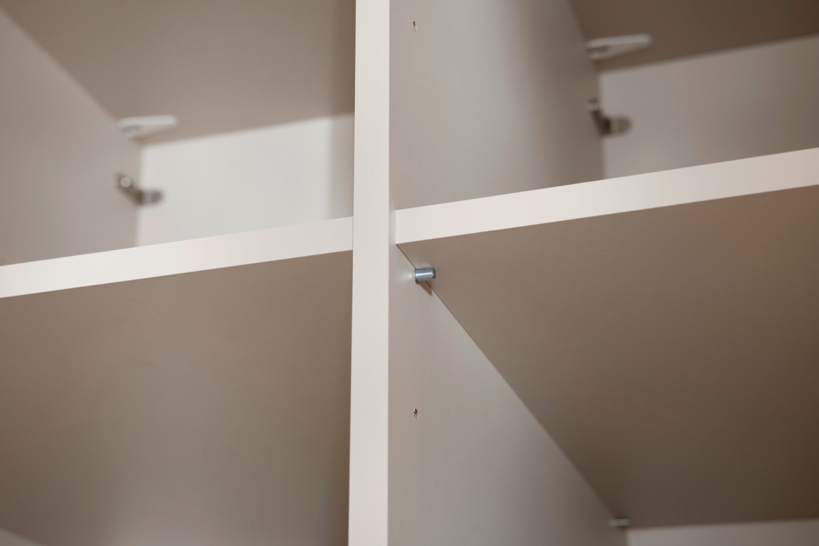 Nahaufnahme eines weißen, vierteiligen Kleiderschranks mit Regalböden, aus der Innenperspektive fotografiert.