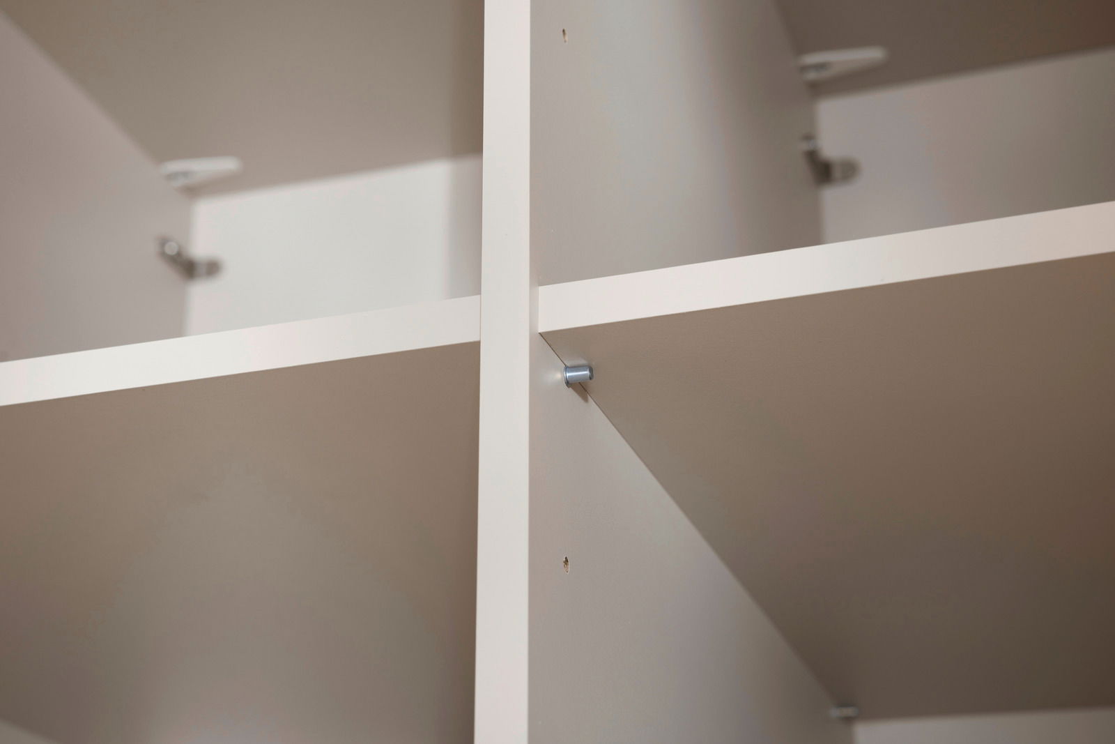 Nahaufnahme eines weißen, vierteiligen Kleiderschranks mit Regalböden, aus der Innenperspektive fotografiert.
