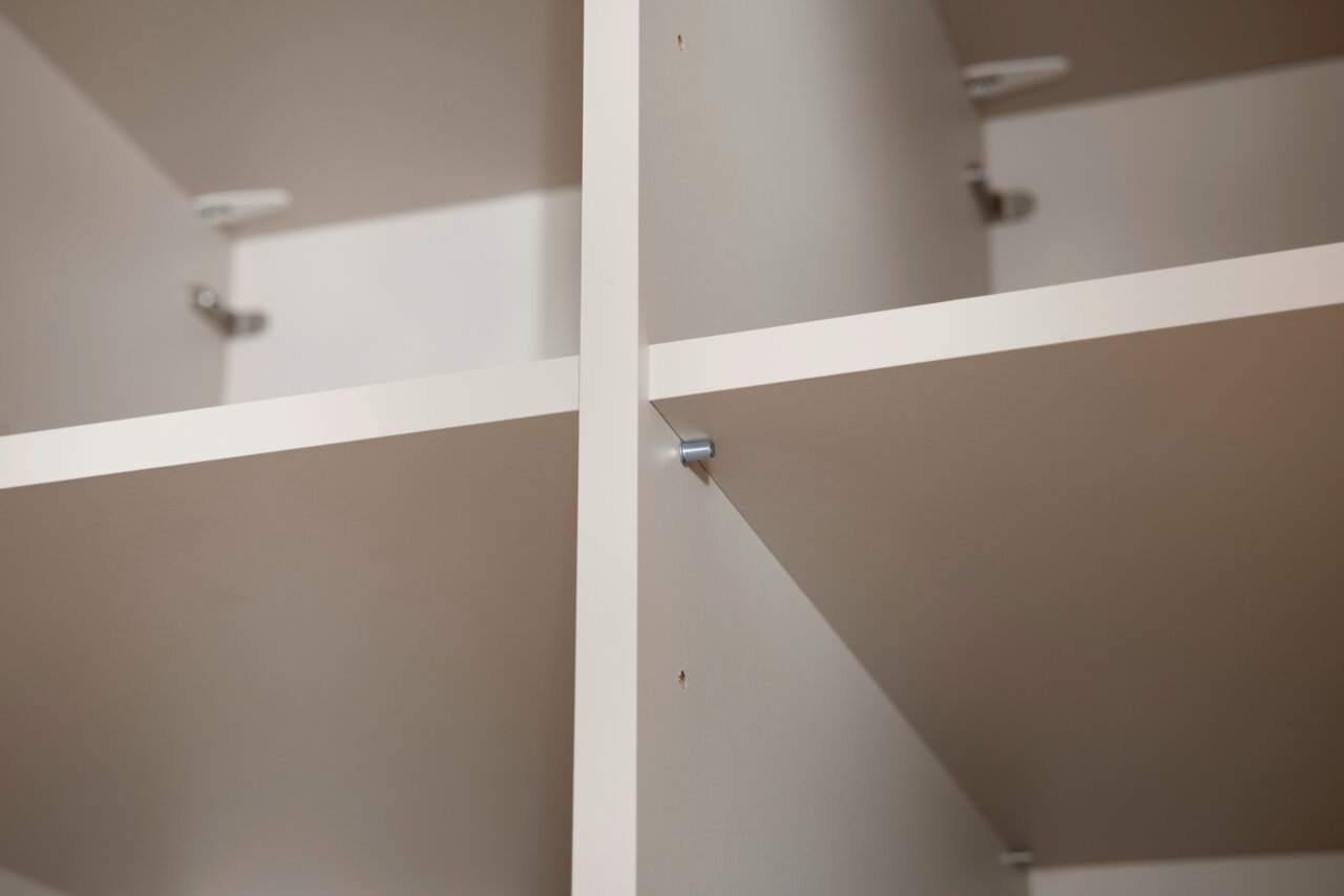 Nahaufnahme eines weißen, vierteiligen Kleiderschranks mit Regalböden, aus der Innenperspektive fotografiert.