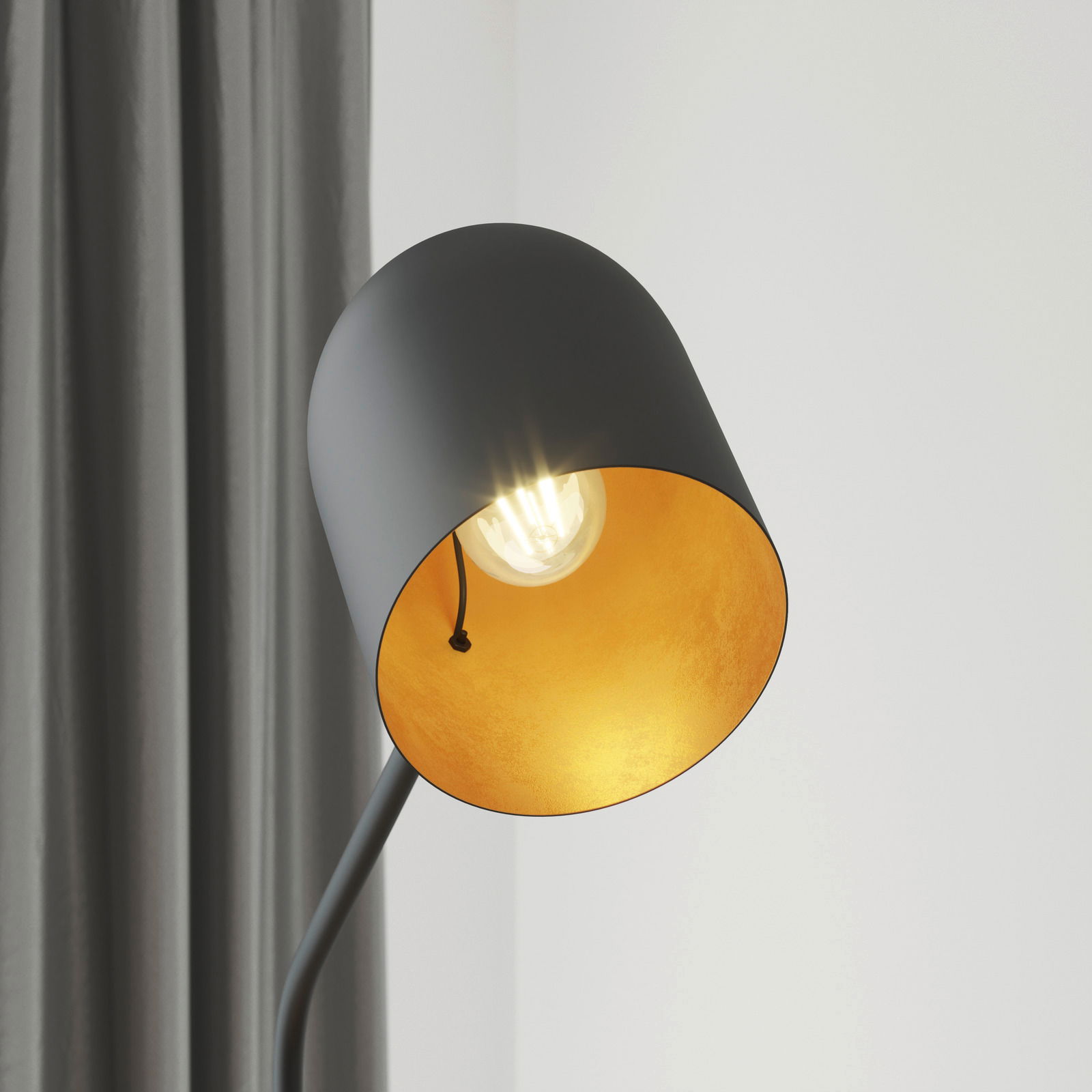 Nahaufnahme einer modernen Stehleuchte mit schwarzem Lampenschirm und goldener Innenseite, die ein warmes Licht ausstrahlt. Perspektive von der Seite.