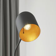 Nahaufnahme einer modernen Stehleuchte mit schwarzem Lampenschirm und goldener Innenseite, die ein warmes Licht ausstrahlt. Perspektive von der Seite.