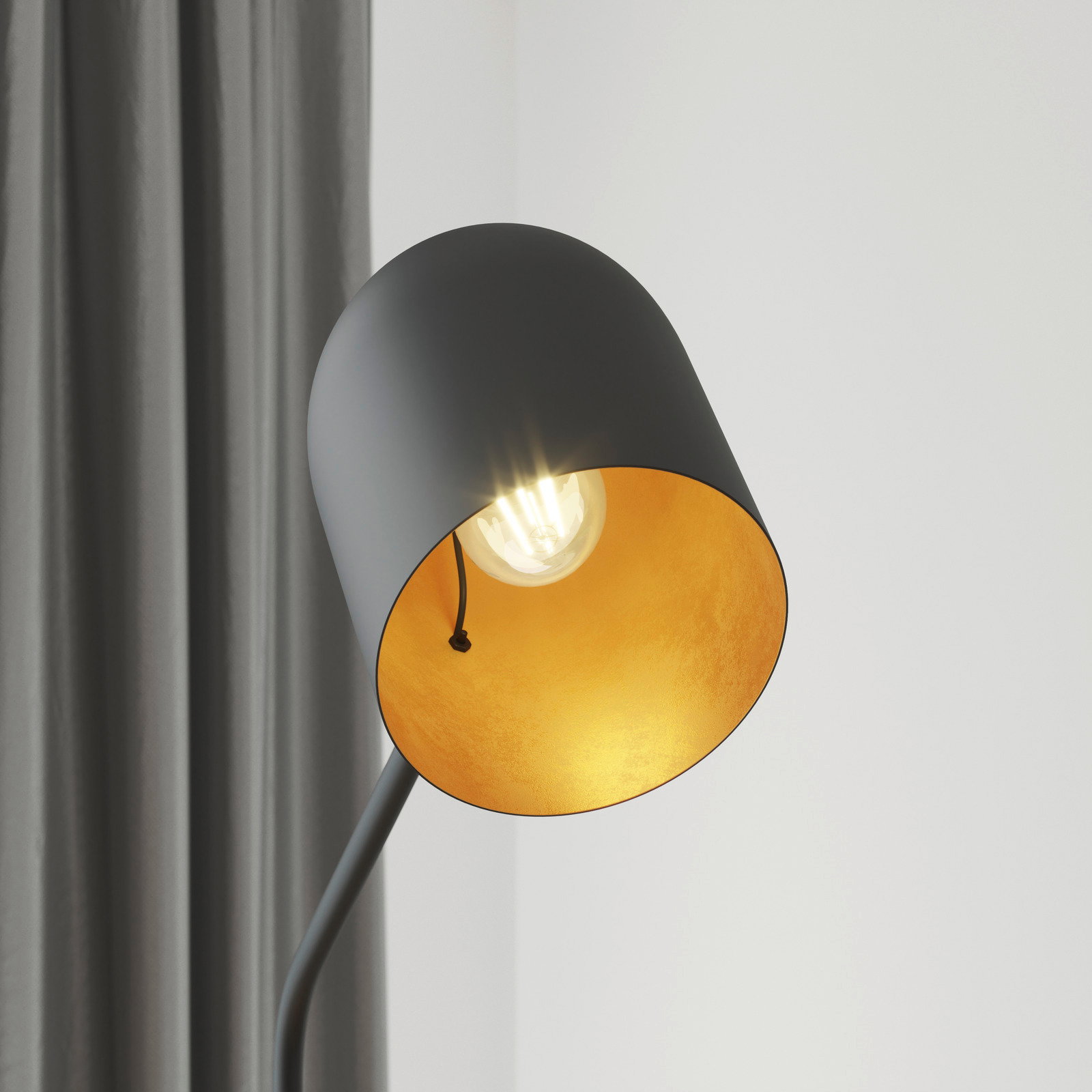 Nahaufnahme einer modernen Stehleuchte mit schwarzem Lampenschirm und goldener Innenseite, die ein warmes Licht ausstrahlt. Perspektive von der Seite.