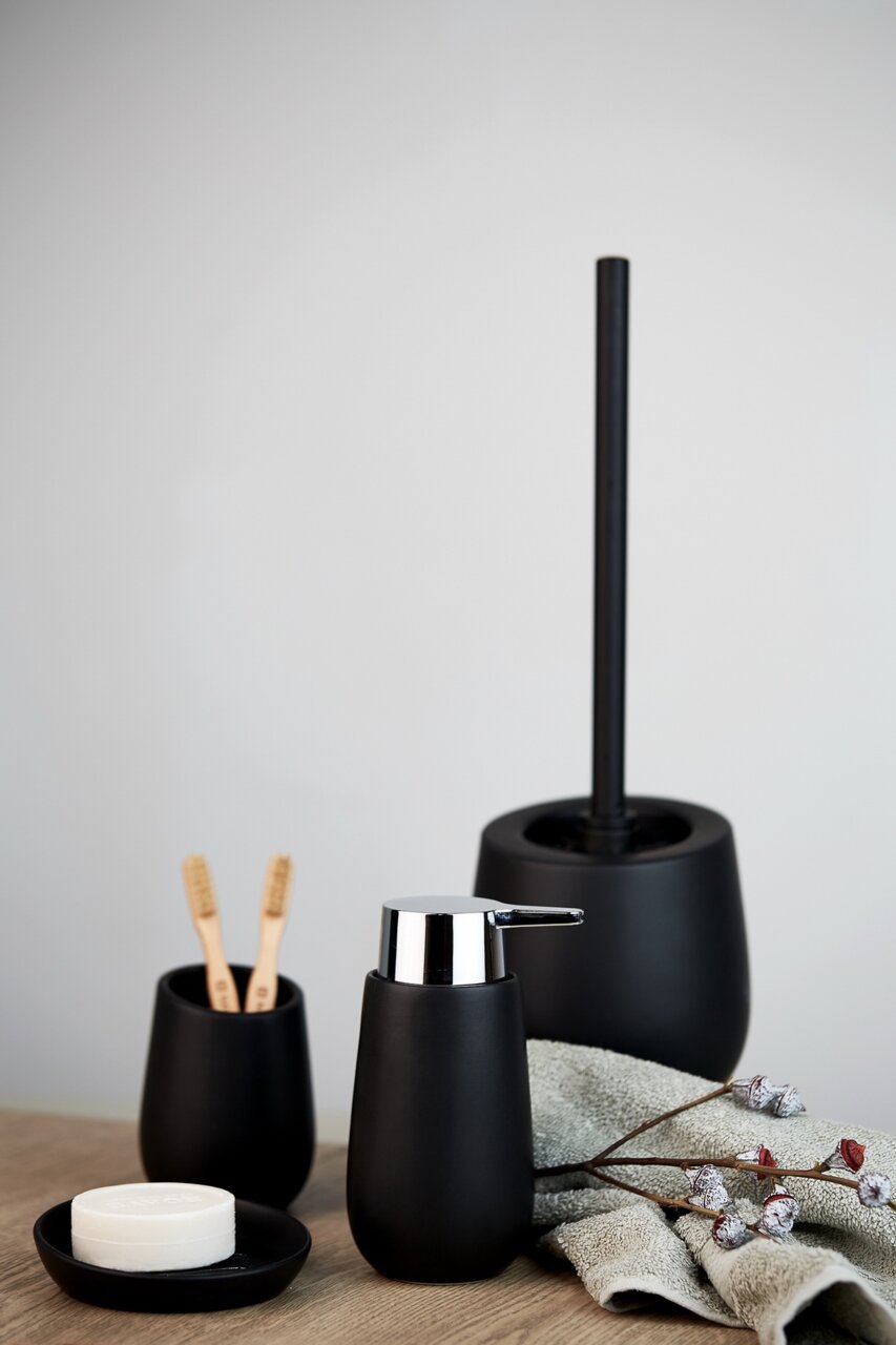 Keramik Seifenspender Badi in mattem Schwarz, frontal fotografiert, neben passendem Zahnbürstenhalter und Toilettenbürste auf einem Holztisch.