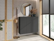 Moderner Hängeschuhschrank in dunklem Design, frontal betrachtet, mit dekorativen Elementen auf der Oberseite, neben einem großen Fenster und einem runden Spiegel.