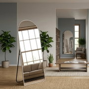 Großer, freistehender Standspiegel mit abgerundetem oberen Rahmen in Weiß, leicht nach hinten geneigt, im Wohnzimmer aus frontaler Perspektive; reflektiert ein Fenster und ein Sofa.