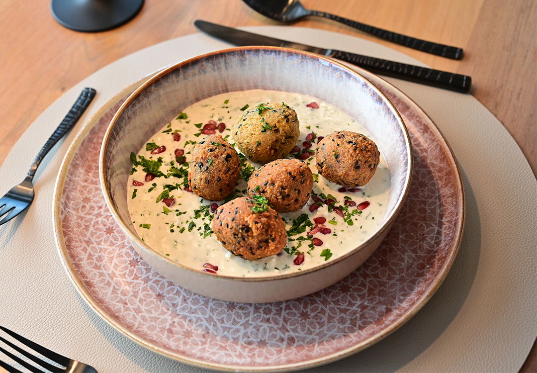 Orientalisches Gericht mit knusprigen Falafel-Bällchen auf Joghurt-Minz-Dip, garniert mit Granatapfel und Kräutern