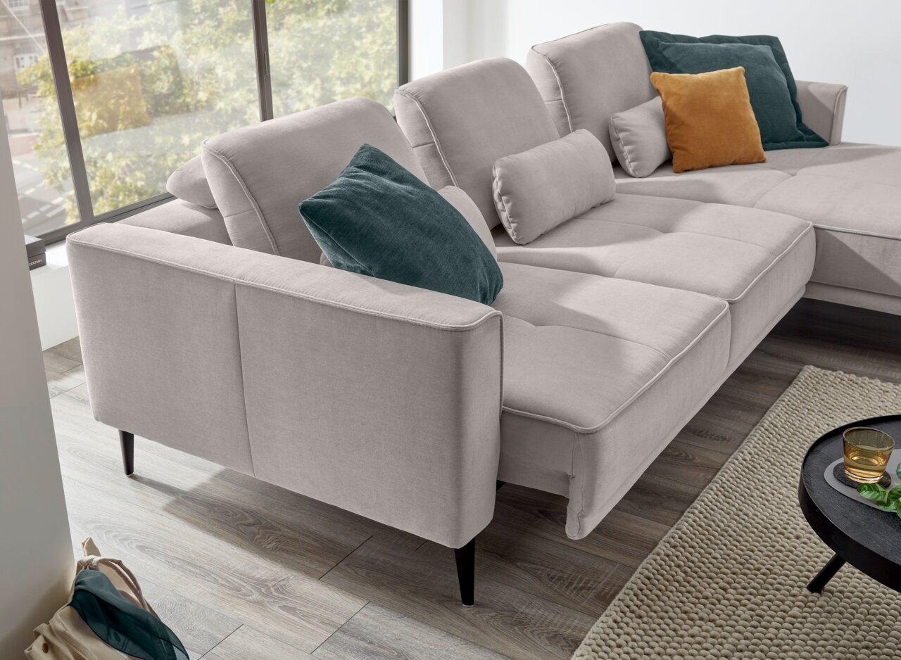 Graues Ecksofa mit mehreren Kissen in verschiedenen Farben, seitliche Perspektive.