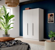 Weißer dreitüriger Kleiderschrank mit langen schwarzen Griffen in modernem Schlafzimmer vor dunkelblauer Wand, Perspektive: frontale Ansicht leicht von links