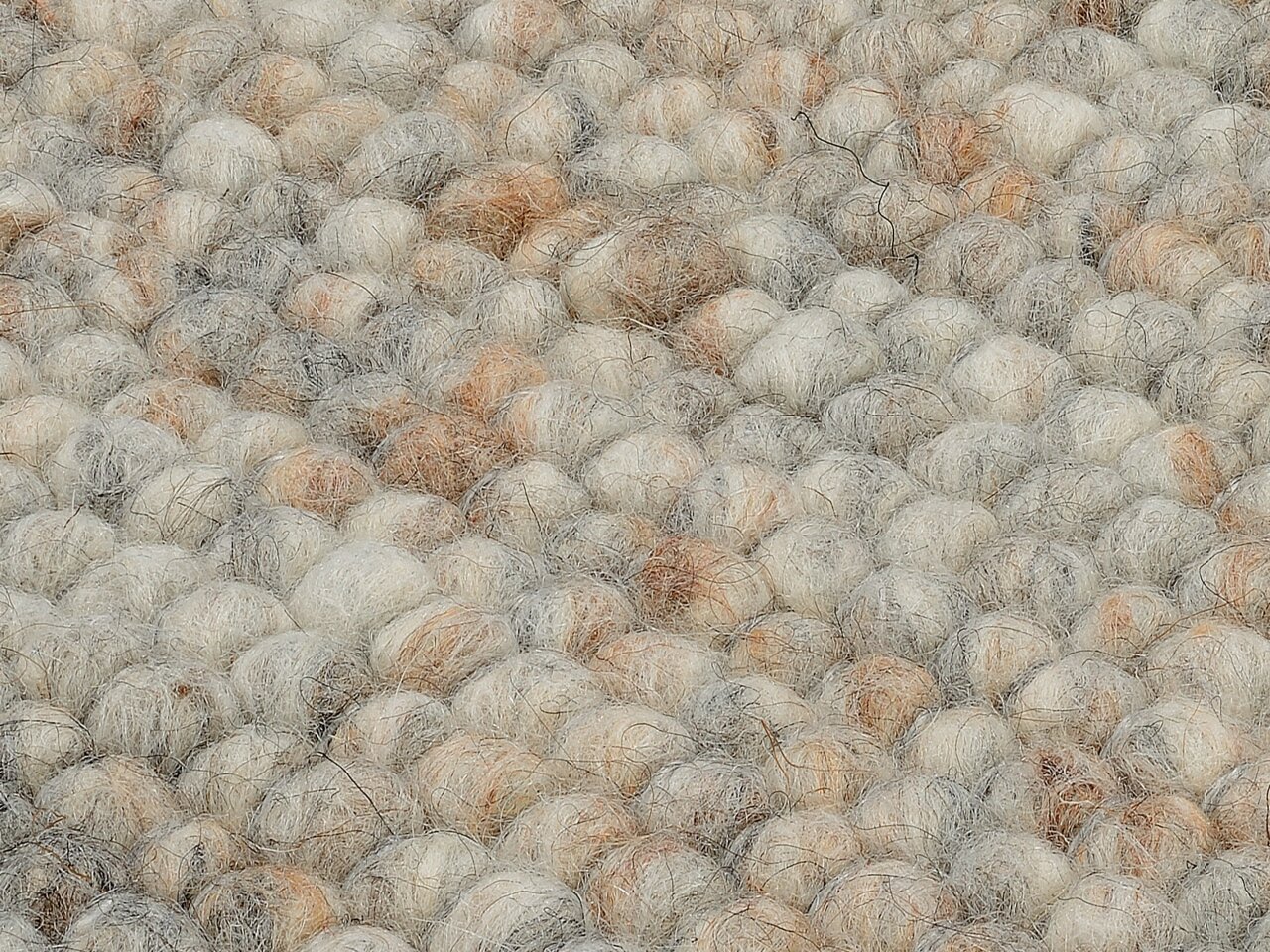 Nahaufnahme eines handgewebten Teppichs mit einer texturierten Oberfläche aus dicken, weichen Wollknäueln in natürlichen Beige- und Grautönen. Die Perspektive zeigt die Struktur des Teppichs von oben.