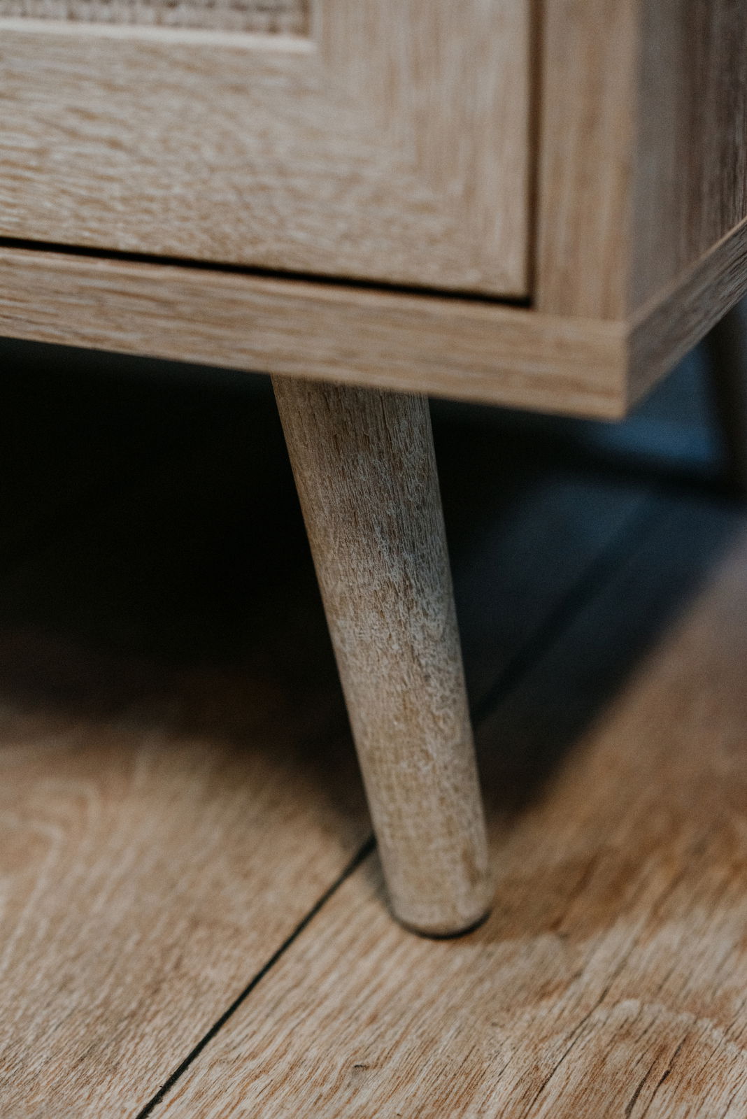 Nahaufnahme eines Holzbeins eines Möbelstücks, das auf einem Holzboden steht. Perspektive von unten.
