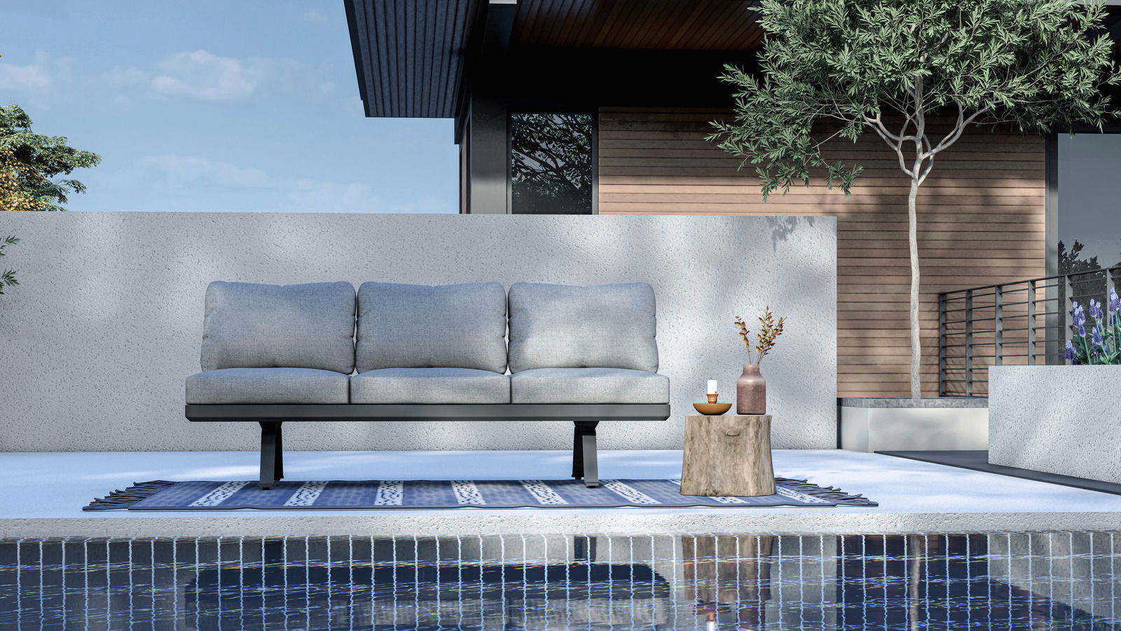 3-Sitzer Loungeelement in moderner Außenumgebung, frontal betrachtet, mit grauen Kissen auf einem blauen Teppich am Pool.