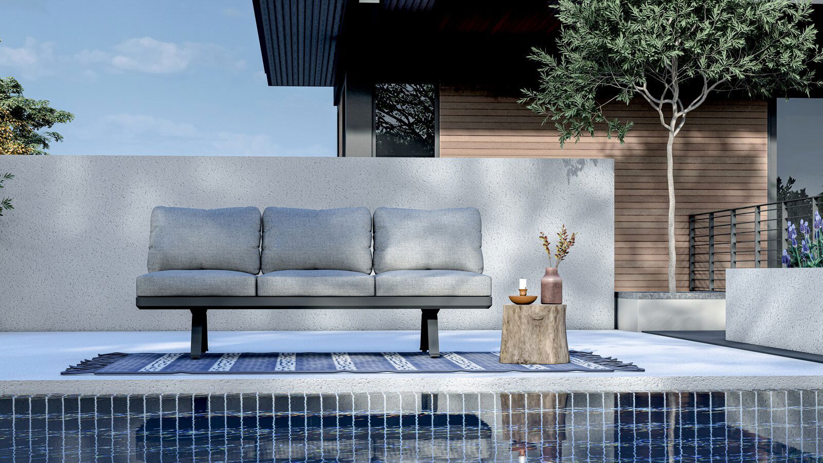 3-Sitzer Loungeelement in moderner Außenumgebung, frontal betrachtet, mit grauen Kissen auf einem blauen Teppich am Pool.