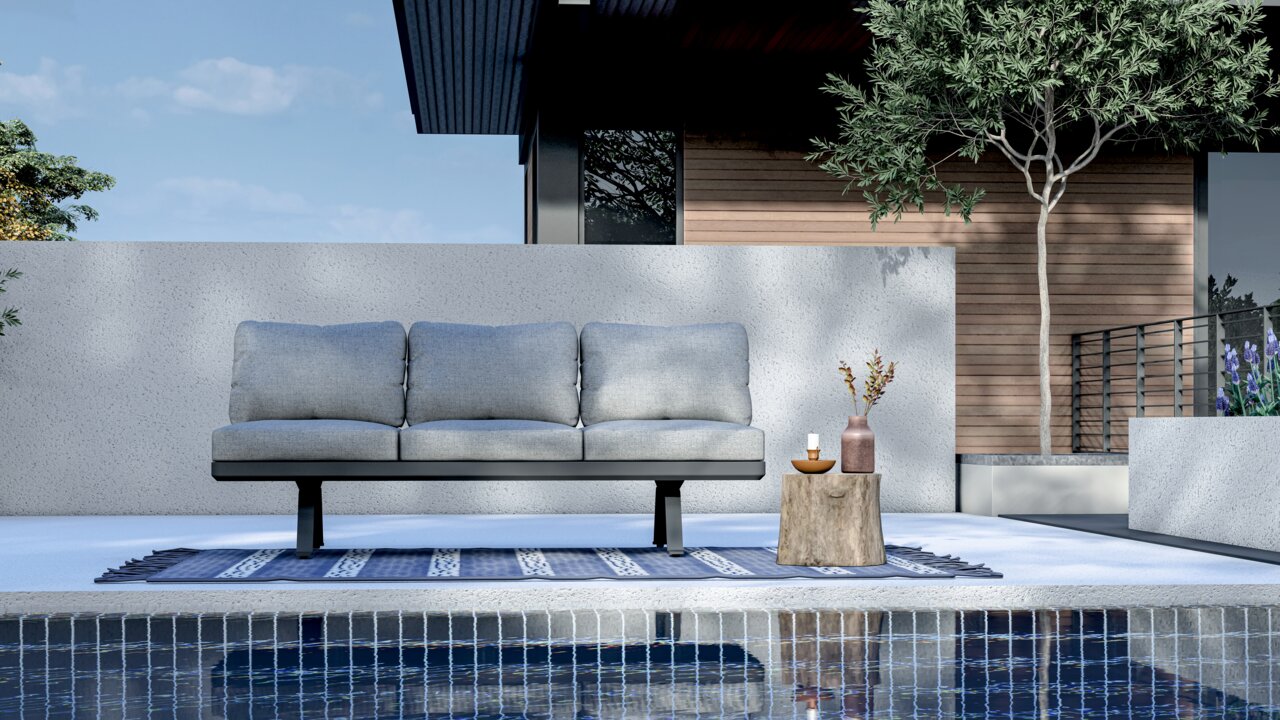 3-Sitzer Loungeelement in moderner Außenumgebung, frontal betrachtet, mit grauen Kissen auf einem blauen Teppich am Pool.