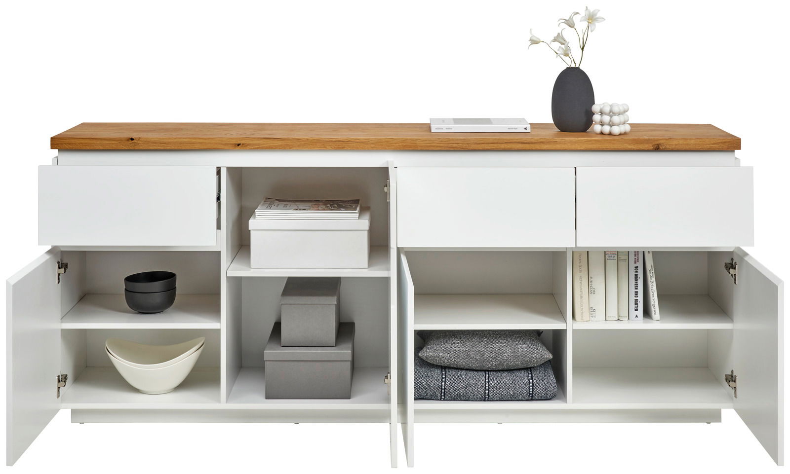 Frontale Ansicht eines weißen XL-Sideboards mit Holztop, offenen Schubladen und Türen, gefüllt mit Büchern, Schalen und Dekoration.
