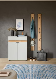 Modernes Flur-Set mit weißem Schuhschrank mit Holz-Akzent, zwei vertikalen Garderobenpaneelen aus Holz mit Haken, aufgehängter Jacke und Cap sowie Tasche und Schuhen auf grauer Wand, Frontansicht.