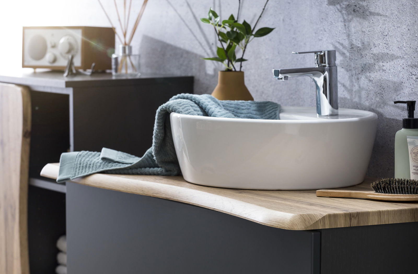 Moderner Waschtisch mit weißem Aufsatzbecken und verchromter Armatur, seitliche Perspektive.