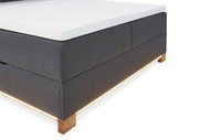 Boxspringbett in dunklem Stoff mit Holzfüßen und integrierter Beleuchtung, seitliche Perspektive