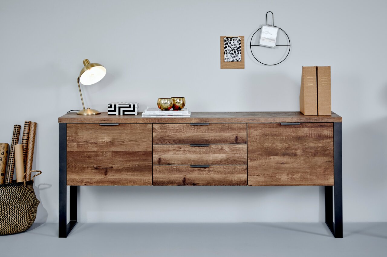 Houten dressoir met metalen poten, gefotografeerd van voren, versierd met een lamp, boeken en decoratieartikelen.