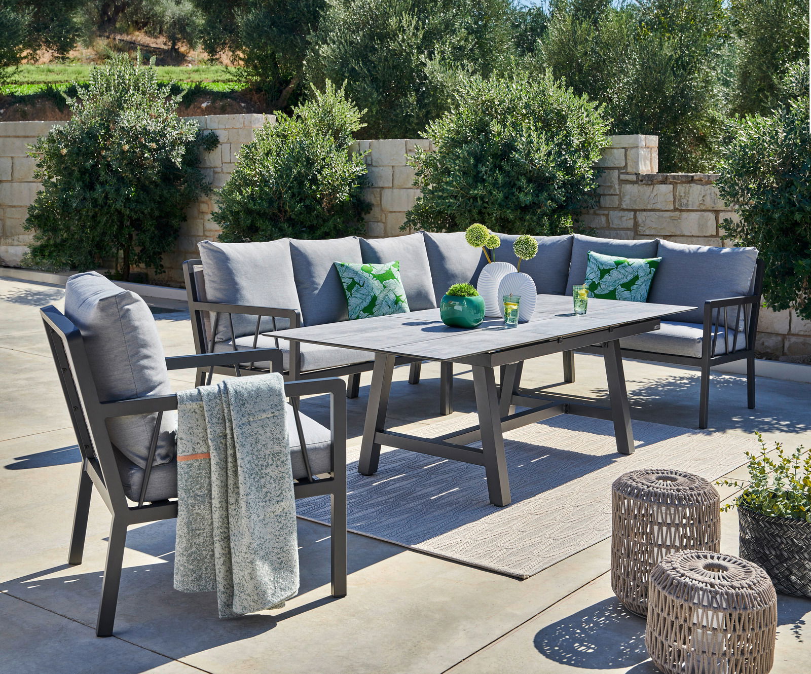 Lounge-Set im Freien mit grauen Kissen, Tisch und dekorativen Elementen, seitliche Perspektive