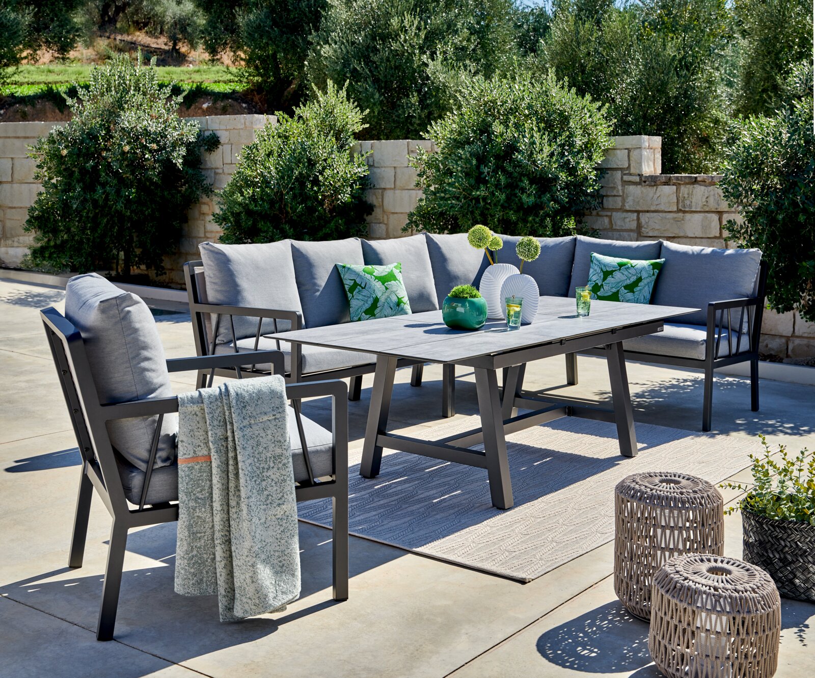 Lounge-Set im Freien mit grauen Kissen, Tisch und dekorativen Elementen, seitliche Perspektive