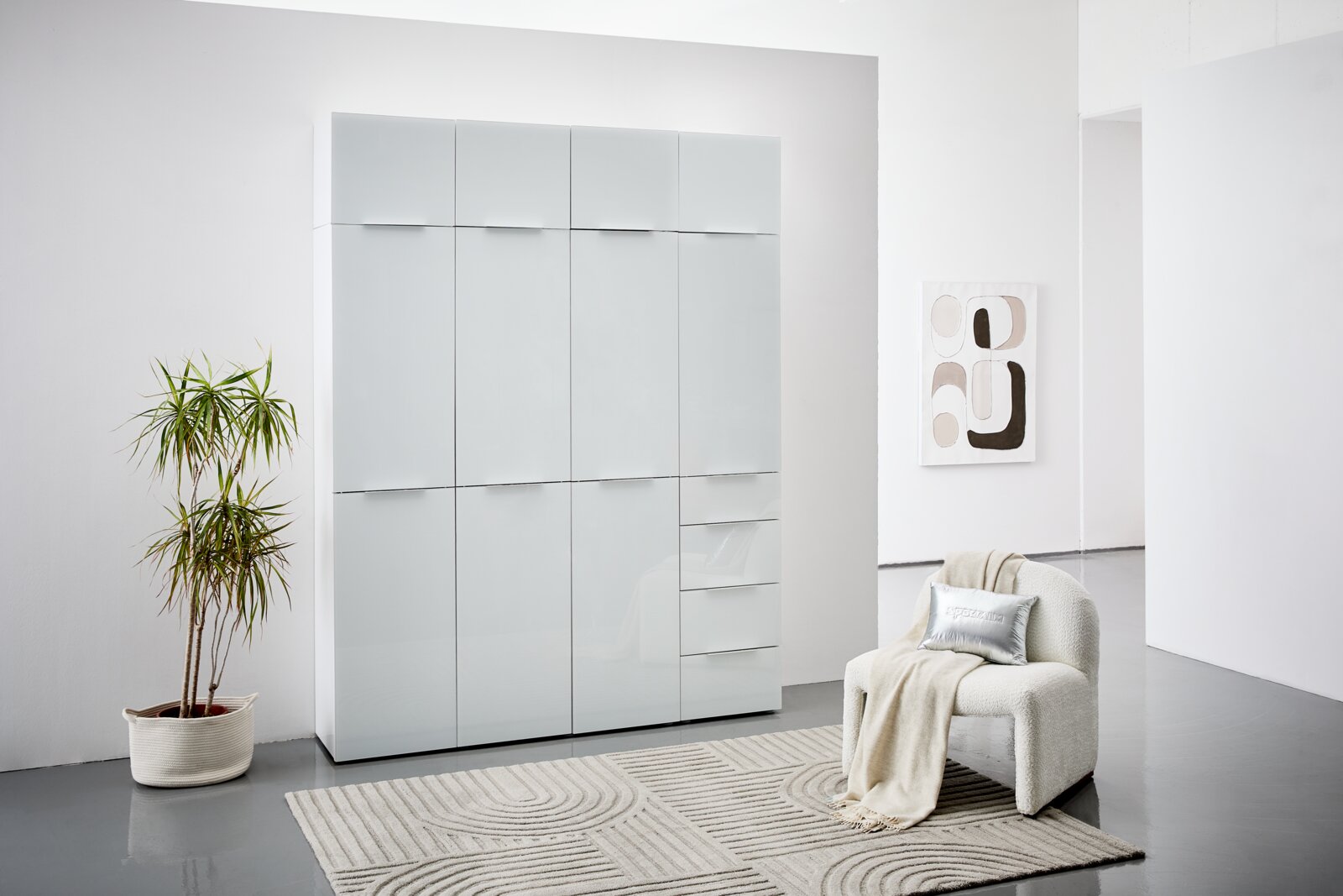 Moderner Mehrzweckschrank mit glänzender Oberfläche, frontal fotografiert in einem stilvoll eingerichteten Raum mit Pflanze und Sessel.