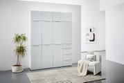 Moderner Mehrzweckschrank mit glänzender Oberfläche, frontal fotografiert in einem stilvoll eingerichteten Raum mit Pflanze und Sessel.