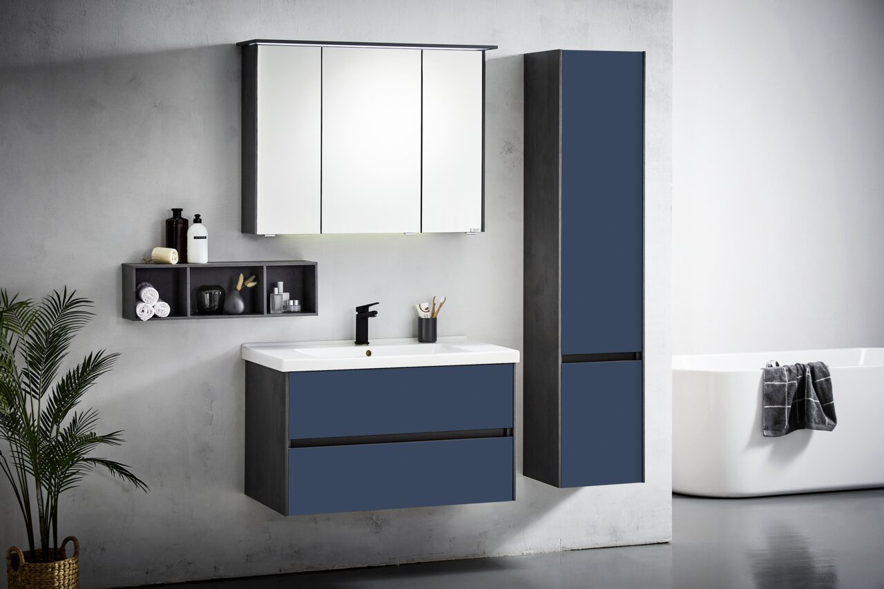 Moderne Badkombination in Dunkelblau mit Spiegelschrank, Waschbeckenunterschrank und hohem Schrank, seitliche Perspektive.