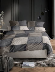 Bettwäsche-Set in modernem, geometrischem Design in Grautönen auf einem Bett in einem stilvoll eingerichteten Schlafzimmer, seitliche Perspektive.
