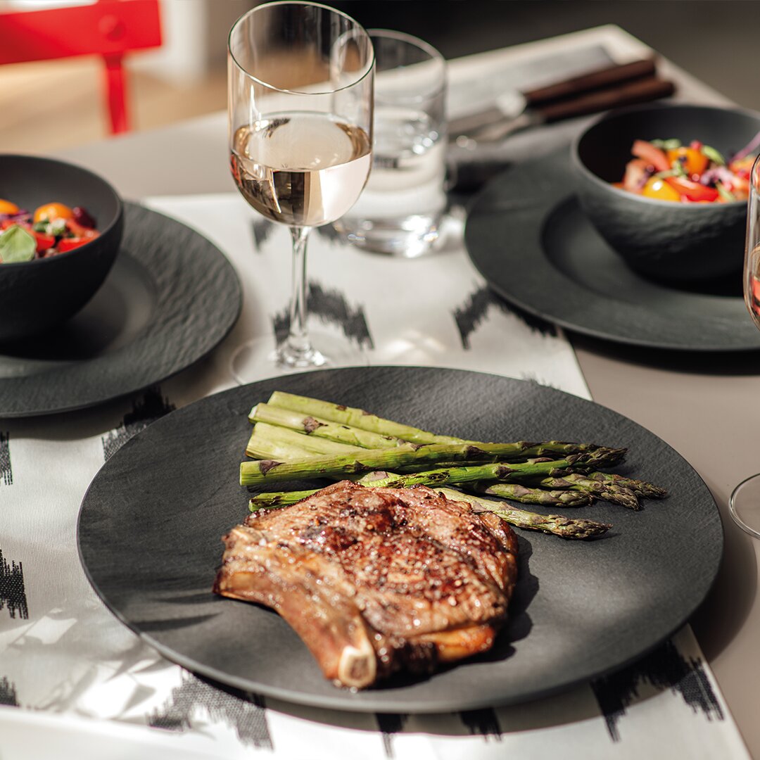 Gourmetteller Manufacture 25cm mit einem saftigen Steak und Spargel, von oben betrachtet, auf einem stilvoll gedeckten Tisch mit Weinglas.