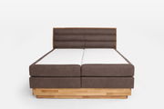 Frontale Ansicht eines Boxspringbetts mit braunem Polsterkopfteil und Holzrahmen.