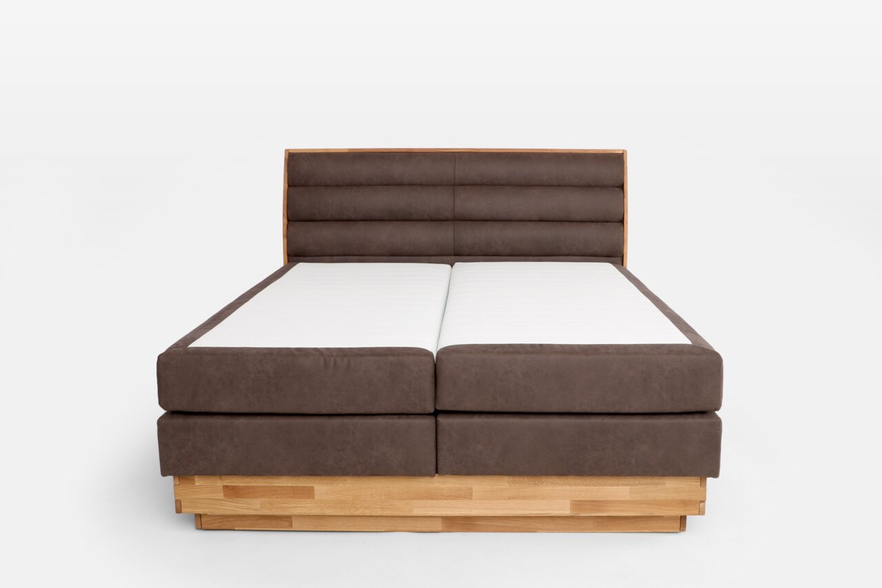 Vooraanzicht van een boxspringbed met een bruin gestoffeerd hoofdeinde en een houten frame.