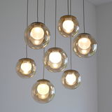 Moderne LED-Pendelleuchte mit sieben kugelförmigen, transparenten Lampenschirmen, von unten betrachtet.