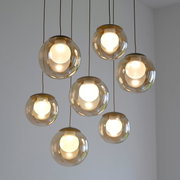 Moderne LED-Pendelleuchte mit sieben kugelförmigen, transparenten Lampenschirmen, von unten betrachtet.