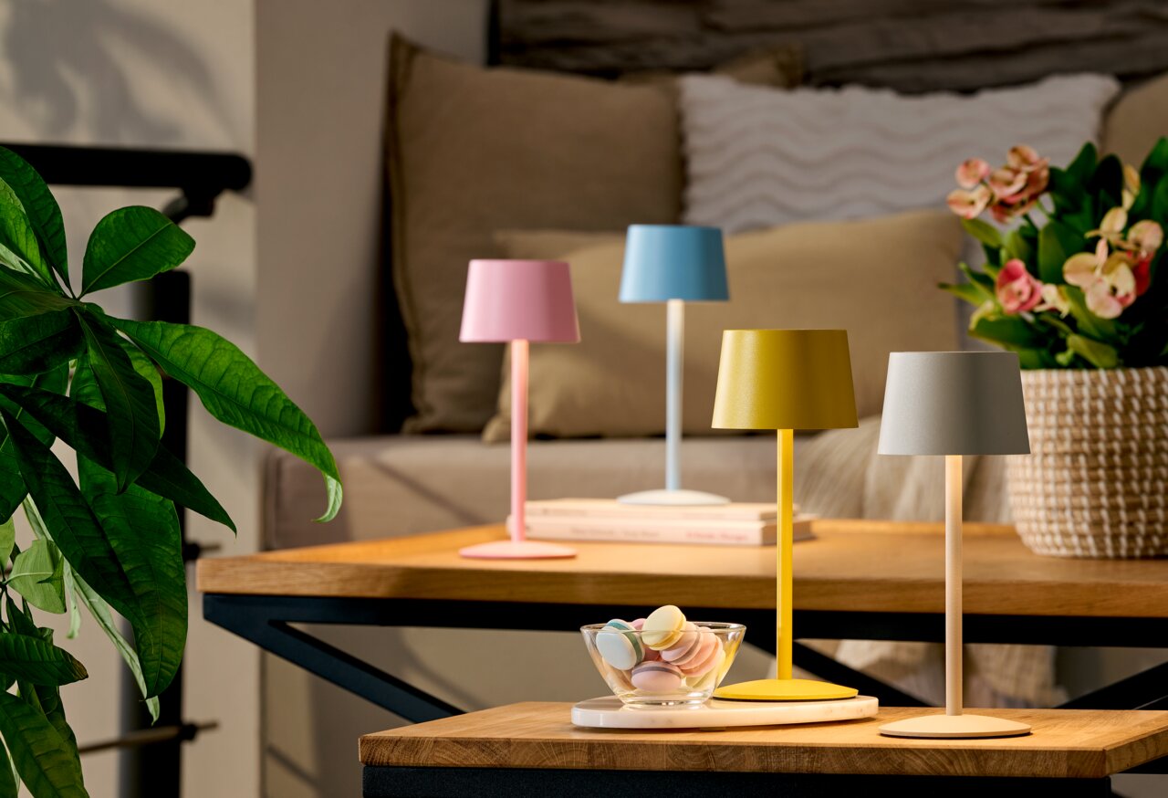 Vier kleine, farbige Tischlampen (rosa, blau, gelb, weiß) auf einem Holz-Couchtisch im Wohnzimmer, Perspektive: leicht erhöhte Frontansicht.