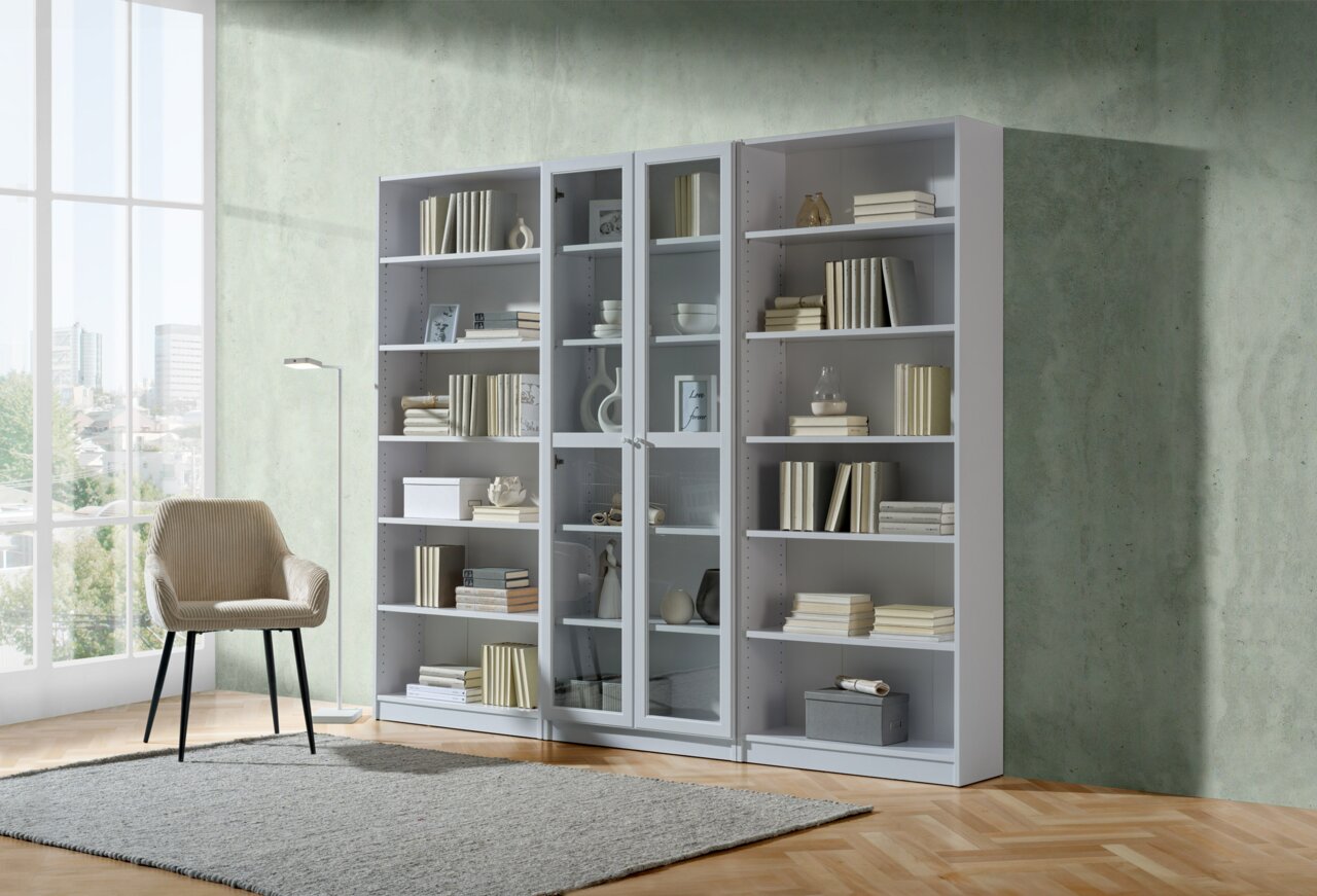 Frontale Ansicht eines modernen weißen Regals mit mehreren Fächern, gefüllt mit Büchern und Dekorationen, neben einem beigen Stuhl in einem hellen Raum.