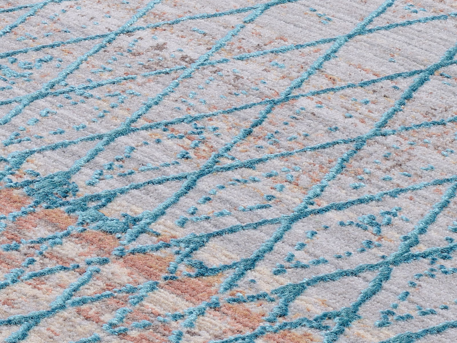 Nahaufnahme eines Designer-Teppichs mit einem modernen, geometrischen Muster in Blau- und Beigetönen, schräg von oben fotografiert.