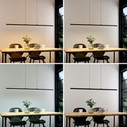 Minimalistische zwarte LED-hanglamp in de vorm van een lange, slanke lichtbalk boven een houten tafel met serviesgoed en een vaas, vooraanzicht van het product.