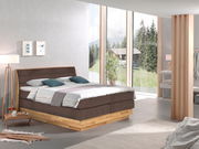 Modernes Boxspringbett in einem hellen, stilvollen Schlafzimmer mit großen Fenstern und Blick auf die Natur, seitliche Perspektive.