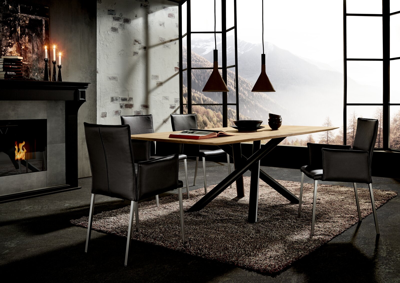Moderner Esstisch mit Holzplatte und schwarzen Metallbeinen, umgeben von schwarzen Stühlen, in einem stilvollen Raum mit Kamin und Bergblick.