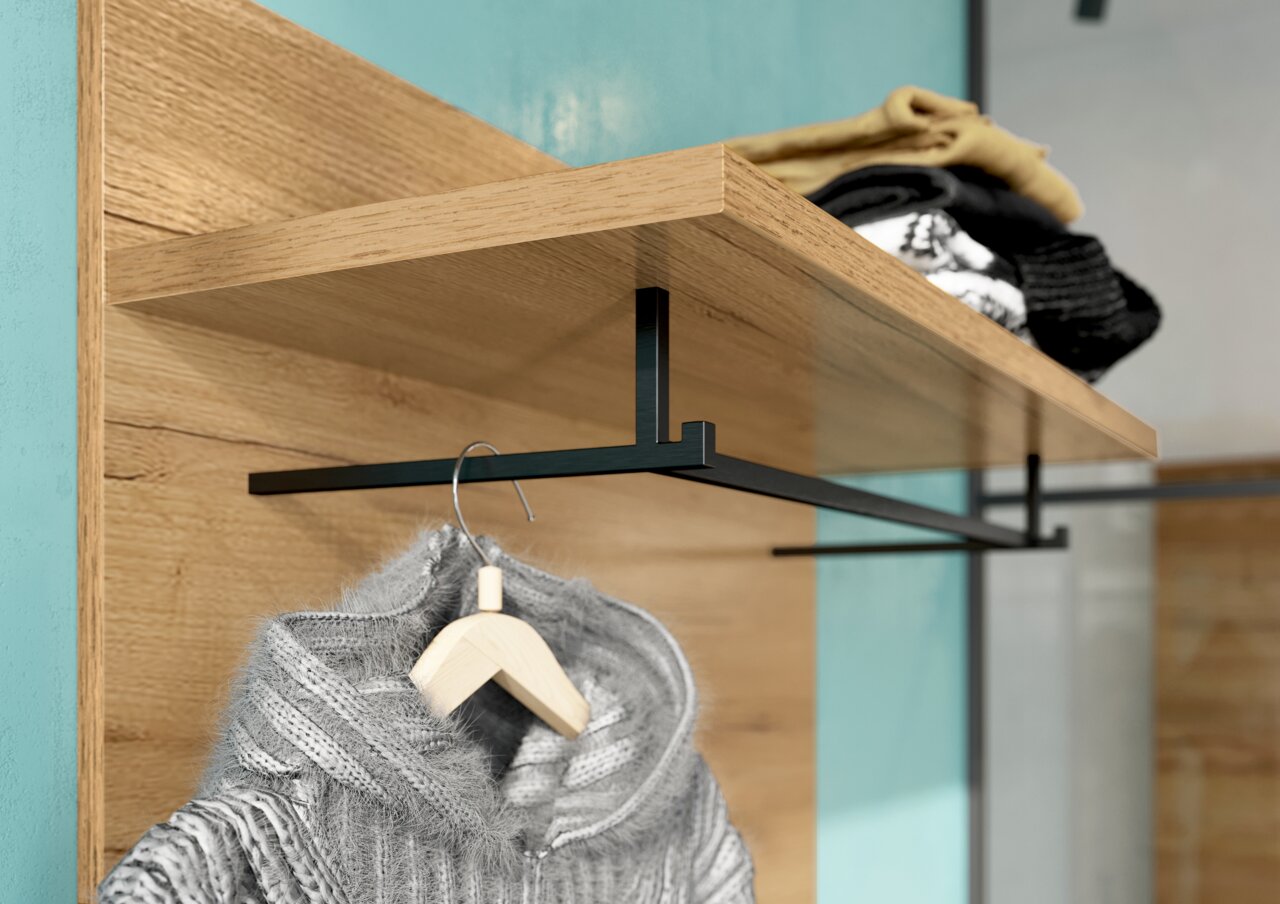 Garderobenpaneel aus Holz mit schwarzer Metallstange, darauf liegende Kleidung und ein hängender Pullover, seitliche Perspektive