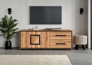 Modern tv-lowboard van licht hout met zwarte handgrepen en twee lades, vooraanzicht in een woonkamer met een aan de muur bevestigde tv.